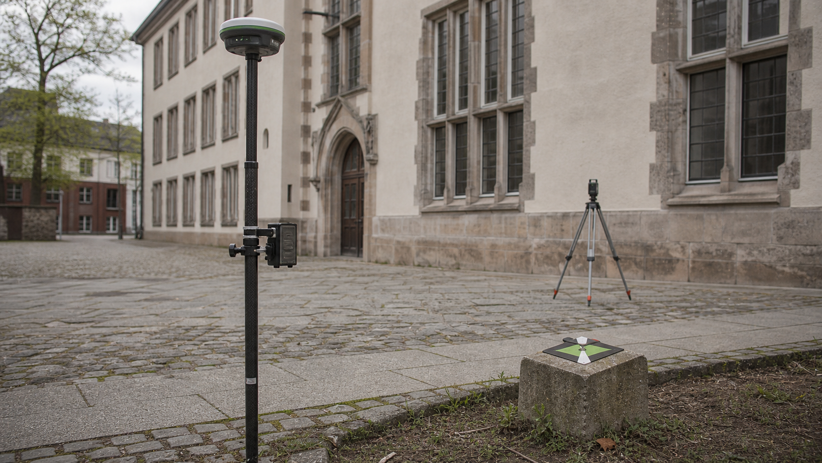GNSS-Rover und Festpunktmarke vor einem Bestandsgebäude
